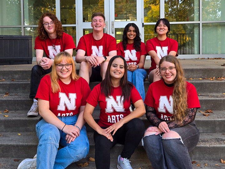 A group of students in matching red Husker t-shirts sit on stairs together.