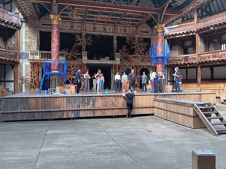 UNL students stand on Shakespeare's Globe Theatre stage blocking in a performance.