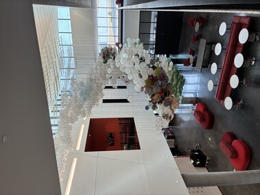 Colorful hanging sculpture in westbrook building atrium with red chairs and tables on polished floors.