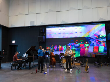 Musicians performing together in a modern studio with colorful projection in the background.