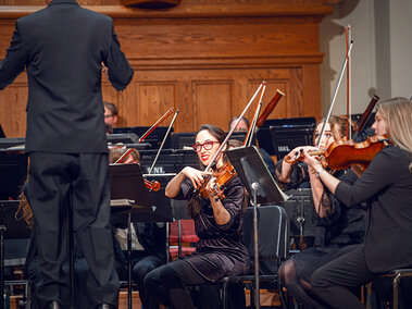 A violinist plays on stage with a symphony.