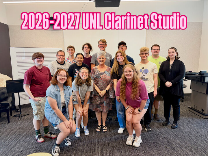 Group photo of 14 smiling people in a music studio, with a woman in the center.