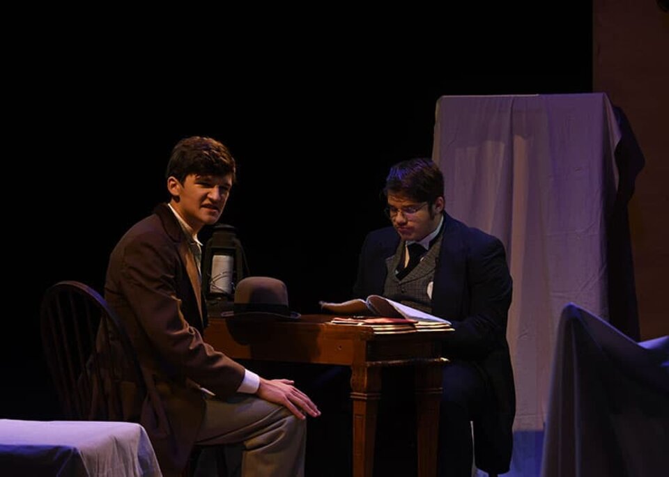 Two men on a darkened stage looking concerned.