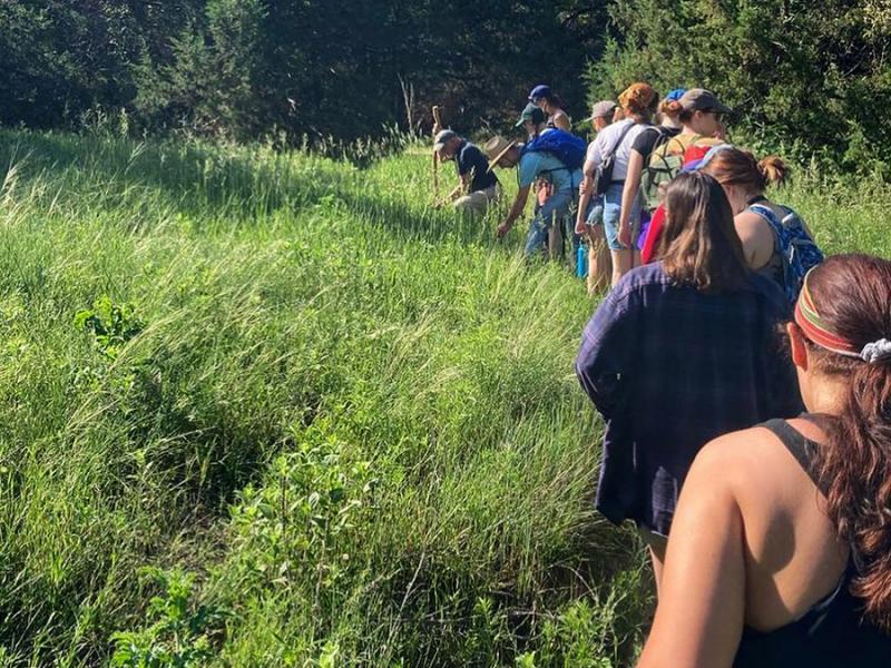 A class of students walking in a line along a nature path in the plains with Professor Aaron Holz leading the group.