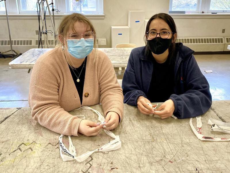 Two Creative Commons members posing for a photo at a table in an art classroom with fiber craft supplies in front of them. 