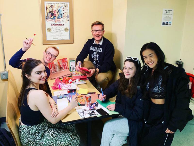 Five members of Nebraska Masquers pose around a booth table for a group picture while they work on fundraising efforts for theatre students.