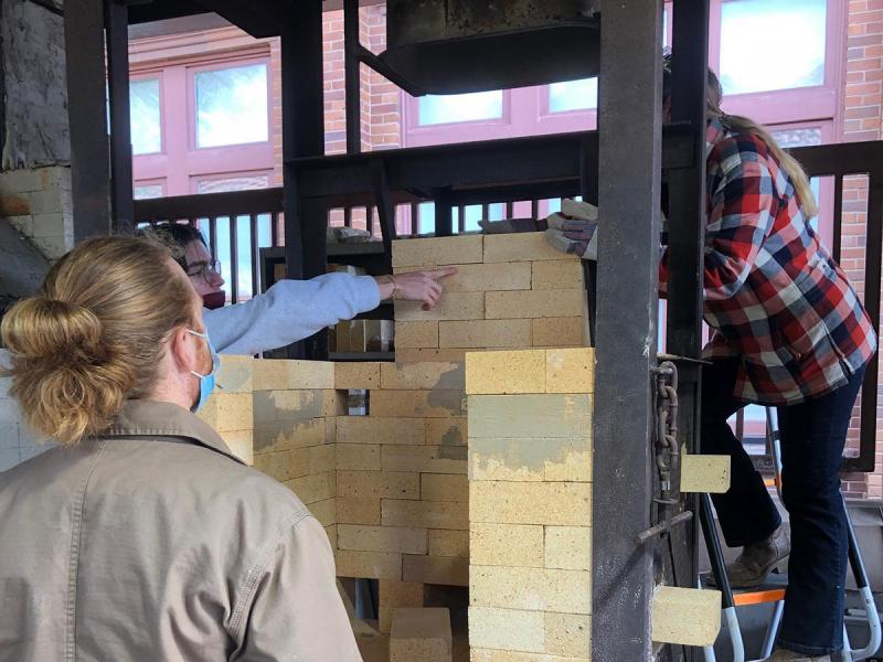 Three School of Art students work together assembling bricks to build a firing kiln.