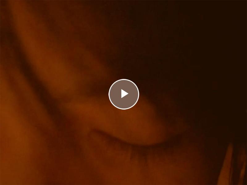 Video still with a play icon over it of a close up of a face with eyes closed.