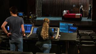 two design tech students work behind the scenes on audio while actors are on stage